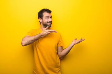 Wall Mural - Man on isolated vibrant yellow color extending hands to the side for inviting to come