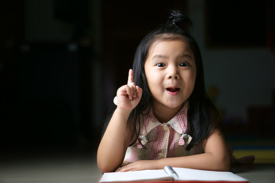 Asian child or kid girl student sleep reading and thinking for new idea with wow open mouth on homework and diary or book at children kindergarten classroom or nursery preschool in home on black space
