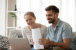 Happy husband and wife read good news online at laptop, millennial couple smiling holding documents receiving positive decision from bank, man and woman get email having mortgage or loan approved