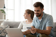 © fizkes - Happy millennial husband enter credit card detail making purchases on internet, dissatisfied wife sitting beside, excited man shopping online spending family money not pay attention to unhappy spouse