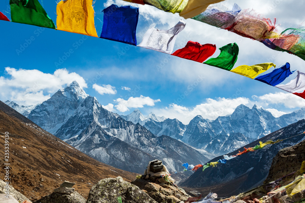 Nepal. From Lukla to Everest. Walk to Everest base camp. Square memorial to the fallen climbers. In the foreground are stones and Nepalese prayer flags, on the horizon of the mountain. - obrazy, fototapety, plakaty 