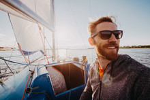 Man Dressed In Casual Wear And Sunglasses On A Yacht. Happy Adult Bearded Yachtsman Close-up Portrait. Handsome Sailor On A Boat Smiling During Regata On A Sea Or River.