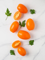 Wall Mural - Orange tomatoes on white marble table. Yellow or orange tomatoes with two half sliced tomato and fresh parsley leaves. Top view or flat lay. Vertical composition.