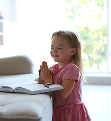 Wall Mural - Cute little girl with beads praying over Bible in living room