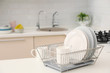Dish drainer with clean dinnerware on table in kitchen. Space for text