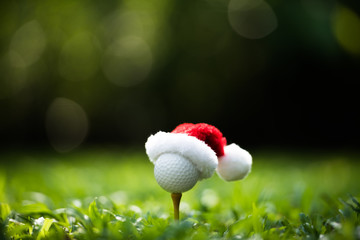 Wall Mural - Festive-looking golf ball on tee with Santa Claus' hat on top for holiday season on golf course background