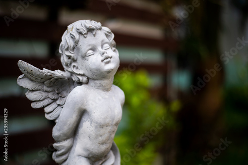 Fotomural closeup cupid sculpture in garden with soft-focus and over light in the backgrou
