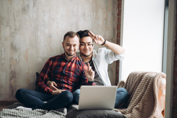 Wall Mural - Handsome caucasian male business partners of non traditional orientation, dressed in casual wear, working on laptop in modern office studio with loft interior and big windows