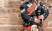 EDINBURGH, SCOTLAND, 24 March 2018 , Scottish Bagpiper Dressed In Traditional Red And Black Tartan Dress Stand Before Stone Wall. Edinburgh, The Most Popular Tourist City Destination In Scotland.
