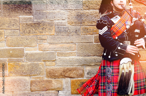 Cuadros en Lienzo EDINBURGH, SCOTLAND, 24 March 2018 , Scottish bagpiper dressed in traditional red and black tartan dress stand before stone wall