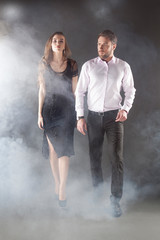 Wall Mural - Romantic pair, handsome man and elegant girl walk in smoke dark studio