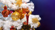 Branch of white artificial Christmas tree decorated with gold and red balls on a blue background. Close up.