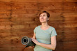 Woman with a yoga Mat on the background of wooden wall