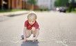 Happy little kid boy drawing with colored chalk on asphalt