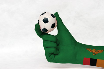 Mini ball of football in Zambia flag painted hand, hold it with two finger on white background. Concept of sport or the game in handle or minor matter. A green field with an orange colored eagle.