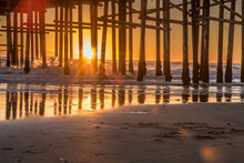 Last Sunlight Fading Behind The Ocean Horizon As Red Glowing Sky Silhouettes The Wooden Pier Pilings At Sunset.
