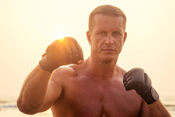 Strong boxer man doing during kickboxing exercise fight with trainer at sunset .close portrait of handsome fitness male model bodybuilder rage, anger and a splash of negative emotions