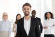 © fizkes - Smiling excited young businessman in suit looking at camera posing with diverse team, millennial professional manager, corporate leader, successful executive, happy ceo or business coach portrait