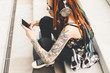 young girl with tattoo and dreadlocks listening to music while sitting on the steps