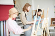© pressmaster - Young man in apron standing by easel between groupmates and painting at lesson in art studio