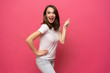 © opolja - Photo of happy young woman standing isolated over pink background. Looking camera showing copyspace pointing.