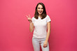 © opolja - Portrait of a smiling happy woman showing victory sign and looking at camera isolated on the pink background.