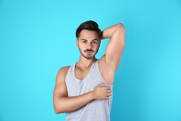 Handsome young man showing armpit on color background. Using deodorant