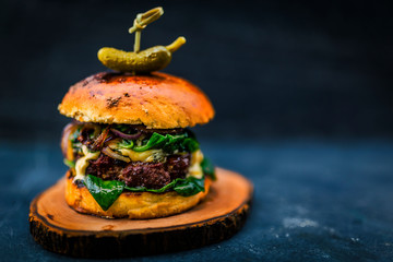 Tasty grilled beef burger with spinach lettuce and blue cheese served on wooden table with copyspace, blackboard in background.