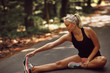 Fit woman warming up with stretches on a forest road