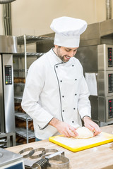 Wall Mural - smiling male baker mashing uncooked dough at kitchen