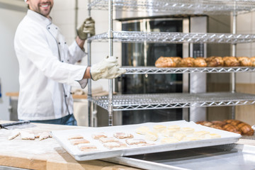 Wall Mural - smiling male baker in white chefs uniform working at kitchen