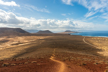 Desert Landscape With A Long Dirt Road Leading Towards Volcano Craters And The Ocean. La Graciosa , Canary Islands, Spain.