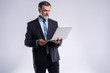 © opolja - Always ready to help you. Confident mature man in formalwear holding laptop and smiling while standing isolated on white background