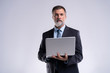 © opolja - Always ready to help you. Confident mature man in formalwear holding laptop and smiling while standing isolated on white background