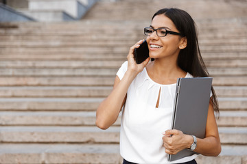 Wall Mural - Beautiful business woman walking outdoors talking by mobile phone.