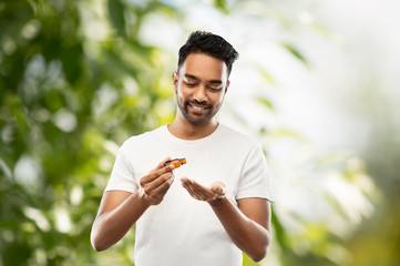 grooming, aromatherapy and people concept - smiling young indian man applying essential oil to his h