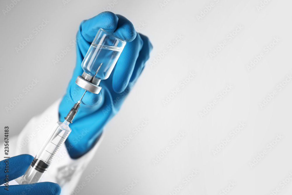 Doctor preparing syringe for injection on light background