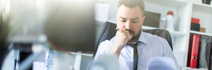 Wall Mural - A man is sitting in the office and scrolls through the documents. photo with depth of field, highlighted focus on man.