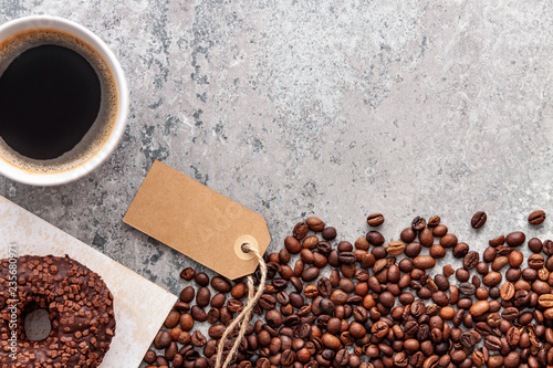 Fotografie, Obraz Donut decorated with dark chocolate balls, roasted coffee beans and cup of coffee on dark gray stone background, top view, copy space