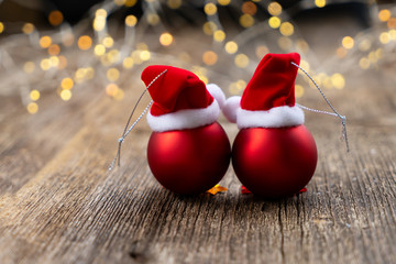 christmas scene with two red balls with santa claus hats and bokeh lights on natural wood background