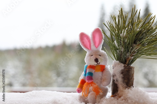 Fotografie, Obraz A white rabbit figurine in a snowdrift against the backdrop of a winter forest