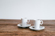 2 Espresso Tassen mit Löffel auf Unterteller Holztisch Hintergrund weiß