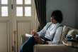© LUMINA IMAGES - Serious middle-aged Asian businessman sitting at cozy armchair and writing in his notebook.