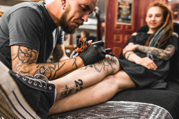 Wall Mural - girl with dreadlocks in a tattoo parlor. The master creates a picture on the body of a young beautiful girl. Close-up of hands and tattoo machine