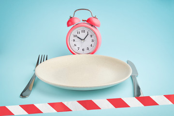 Alarm clockб plate with cutlery and barrier tape. Concept of intermittent fasting, lunchtime, diet and weight loss