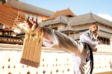 Wall Mural - Female in kimono practicing taekwondo. Breaking board