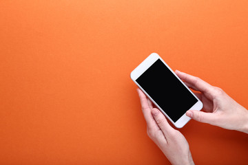 Fototapete - Female hands holding smartphone on orange background