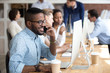 © fizkes - Smiling confident African American man talking, consulting by phone with client, customer, using computer, looking at screen, reading, checking, searching information in internet