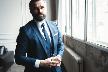 Wall Mural - Stylish young man in suit and tie. Business style. Fashionable man in full suit looking in camera while standing indoors.