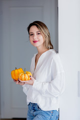 Young caucasian woman in white shirt and blue jeans with pumpkins at home